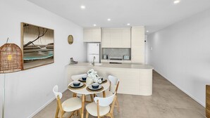 Una cocina moderna con armarios blancos, una isla central y un comedor con una mesa redonda y sillas.