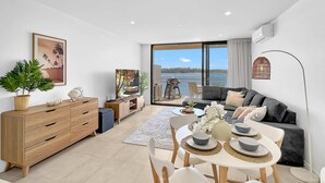 Una sala de estar moderna con comedor, un ventanal con vista al mar y un rincón de descanso acogedor.