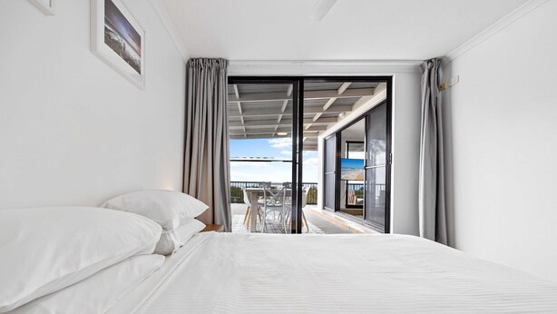A bedroom with a large bed, a view of the balcony, and a sliding glass door. - Beachside 3-bed With Bbq, Pool, Gym (Sunshine Coast)
