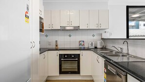 A modern kitchen with white cabinets, a built-in oven, a dishwasher, and a sink. - Beachside 3-bed With Bbq, Pool, Gym (Sunshine Coast)