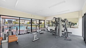 A gym with various exercise equipment, large windows, and a view of a pool. - Beachside 3-bed With Bbq, Pool, Gym (Sunshine Coast)