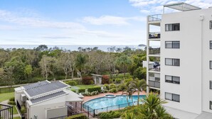 A modern building with a rooftop pool, surrounded by lush greenery and a view of the sea. - Beachside 3-bed With Bbq, Pool, Gym (Sunshine Coast)