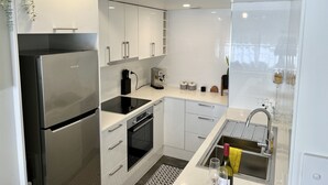 Une cuisine moderne avec des meubles blancs, un réfrigérateur en acier inoxydable, une machine à café et un évier avec des verres à vin.