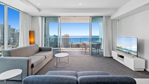 Une chambre d’hôtel moderne dotée d’un balcon, d’un canapé, d’une télévision et offrant une vue sur la ville et l’océan.