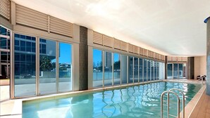 Une piscine intérieure avec des parois en verre transparent, un sol carrelé et un escalier en métal.