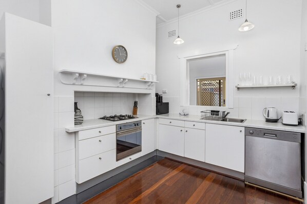 Een moderne keuken met witte kastjes, een gasfornuis, een oven, een vaatwasser en een magnetron.