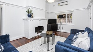 A living room with a fireplace, blue sofas, a black TV stand, and a floor lamp. - Chic Semi-detached 2-bed Home With Outdoor Dining (Perth)