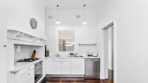 A modern kitchen with white cabinetry, a gas stove, an oven, a dishwasher, and a microwave. There is a clock on the wall and pendant lights above the counter. - Chic Semi-detached 2-bed Home With Outdoor Dining (Perth)
