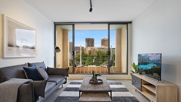 Un salon moderne comprenant un canapé, une table basse et un meuble pour la télévision, avec une grande fenêtre offrant une vue sur la ville.
