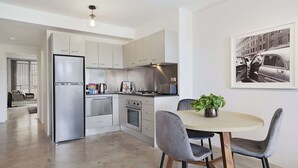 Une cuisine moderne dotée d’appareils électroménagers en acier inoxydable, un coin repas avec une table ronde et des chaises, et un tableau encadré au mur.