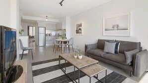 Un salon moderne avec un canapé gris, une table basse et un coin repas comprenant une table et des chaises blanches.