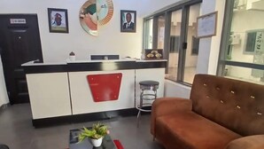 Un salon moderne avec un tapis rouge, un canapé marron, une petite table sur laquelle est posée une plante, et un coin cuisine avec un comptoir et des placards.