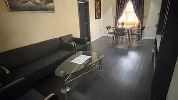 Una sala de estar con un sofá de color oscuro, una mesa de centro de vidrio y un comedor con mesa y sillas.