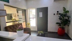 Un espace d’accueil au design moderne, comprenant un comptoir de réception, un coin salon confortable et une grande plante en pot.