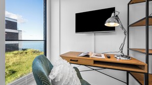 A modern room with a desk, a chair, a TV, and a view of the sea.
