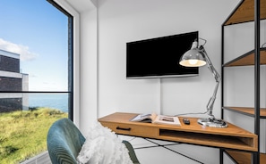 Quarto moderno com escrivaninha, cadeira, televisão na parede e vista para o mar.