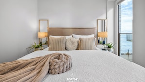Una camera d'albergo con un letto grande, due abat-jour, una testiera in legno e vista mare da una finestra ampia.