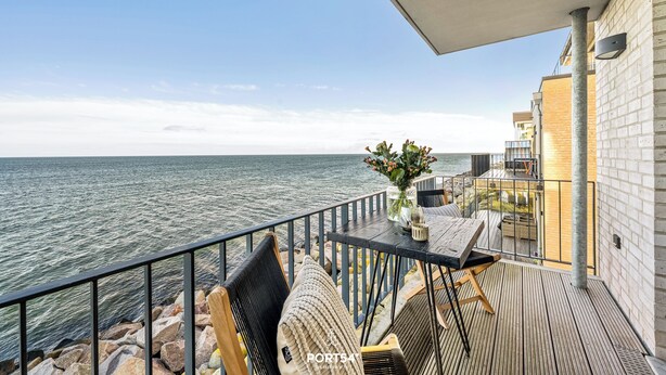 Un balcone con vista sul mare, con un tavolo, sedie e un vaso di fiori.