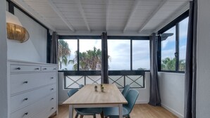 A room with a wooden table, two blue chairs, a white dresser with drawers, and large windows with curtains. - Casa Ondina - Shared pool and Sea view By LVH (Puerto del Carmen)