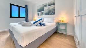 A neatly made bed with white linens and blue accents, a bedside table with a lamp, and a wall with framed pictures. - Casa Ondina - Shared pool and Sea view By LVH (Puerto del Carmen)