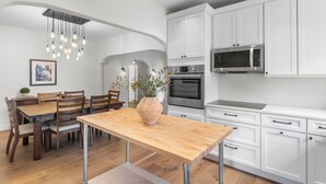 A modern kitchen with white cabinets, stainless steel appliances, and a wooden dining table. - Original Davis Islands Spanish Mission Bungalow (Tampa)