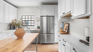 A modern kitchen with white cabinetry, a stainless steel refrigerator, and a wooden dining table. - Original Davis Islands Spanish Mission Bungalow (Tampa)