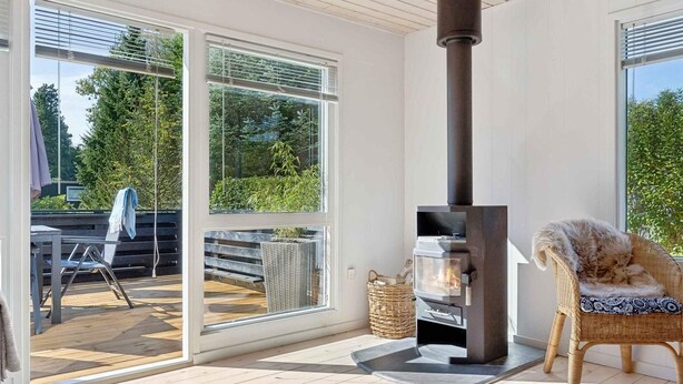 A modern outdoor patio with a wood-burning stove, wicker furniture, and a glass door leading to a deck.