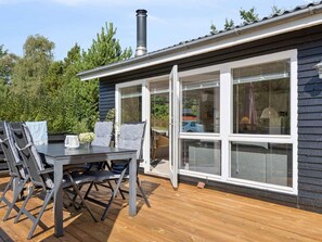 A deck with a table and chairs, a chimney, and a house with large windows. - 4 Star Holiday Home in Hals (Hals)