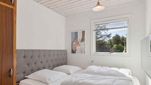 A bedroom with a large bed, a window with a view of trees, and a pendant light.