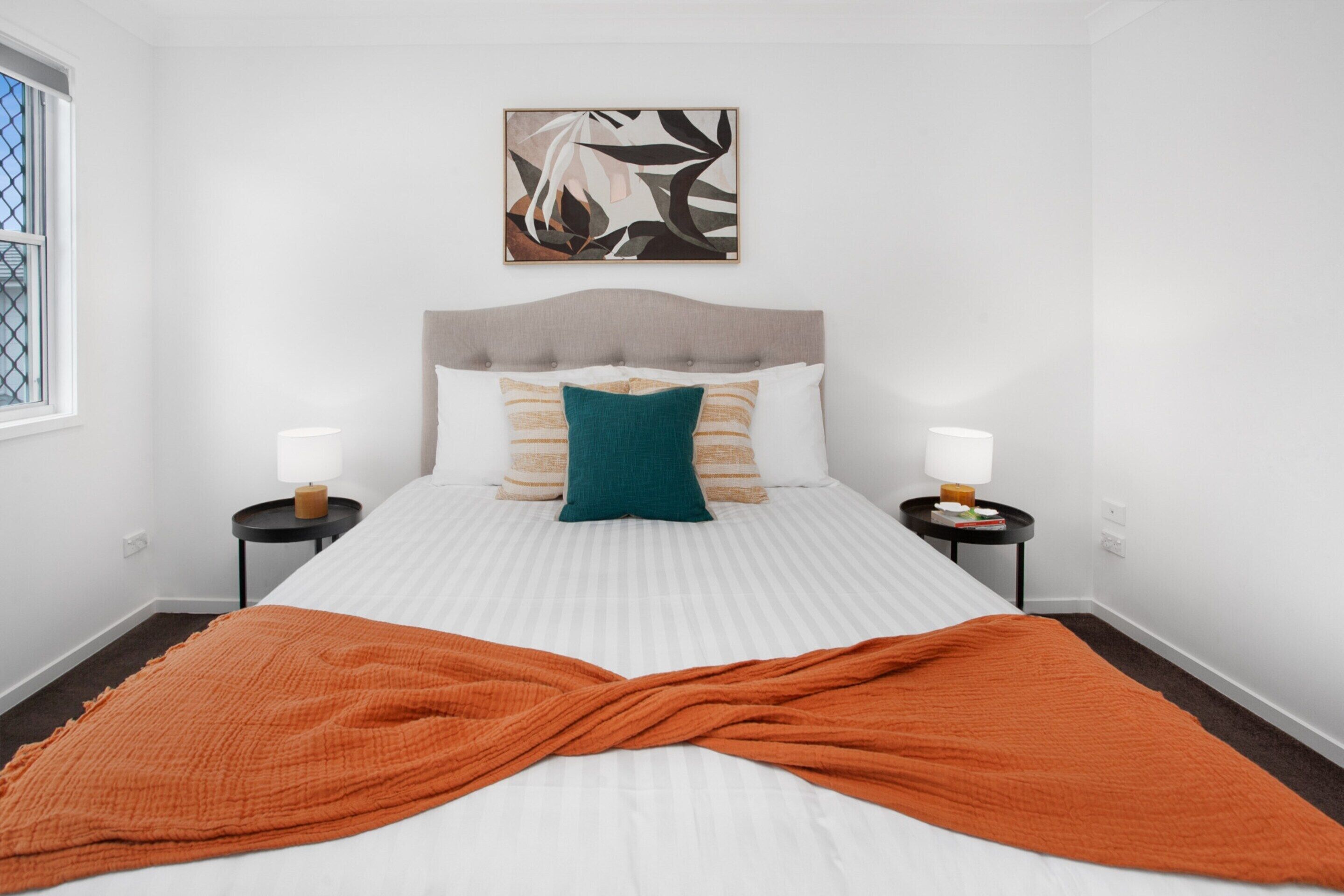 A hotel room with a large bed, two bedside tables, a window, and a wall-mounted artwork.