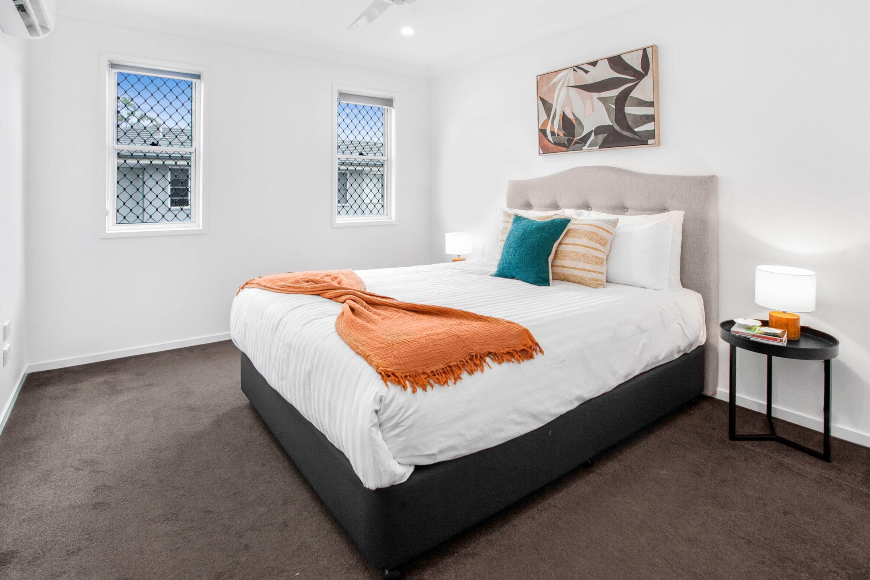 A bedroom with a bed, two bedside tables, a window, and a painting on the wall.