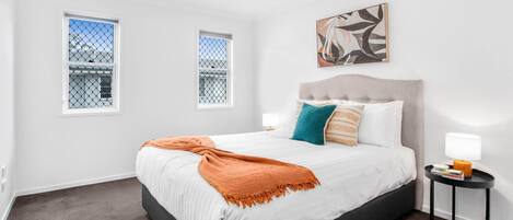 A bedroom with a bed, two bedside tables, a window, and a painting on the wall.