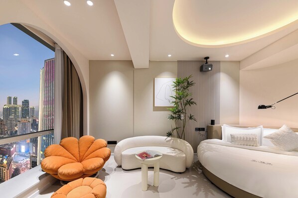 A modern bedroom with a curved bed, a small white table, and a large window offering a city view. - Liberation Monument Riverside HoteL (Chongqing)