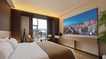 A hotel room with a large bed, a desk, a television, and a view of a cityscape.