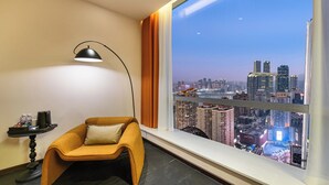 A hotel room with a large window offering a city view, a comfortable armchair, a side table with a lamp, and a tray with items. - Liberation Monument Riverside HoteL (Chongqing)