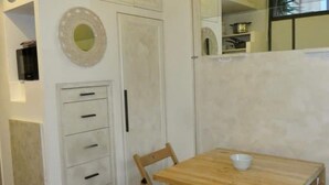 A room with a wooden table and a chair, a white cabinet with drawers, and a round mirror on the wall. - Cozy Independent House with Large Terrace in Heart of Monti (Roma)