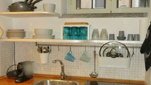 A kitchen with a stainless steel sink, a coffee maker, and various kitchen utensils and dishes on shelves. - Cozy Independent House with Large Terrace in Heart of Monti (Roma)