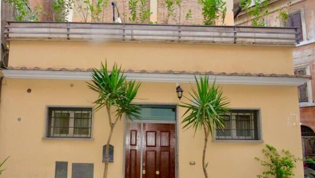 A two-story building with a brown door, two windows, and potted plants. - Cozy Independent House with Large Terrace in Heart of Monti (Roma)