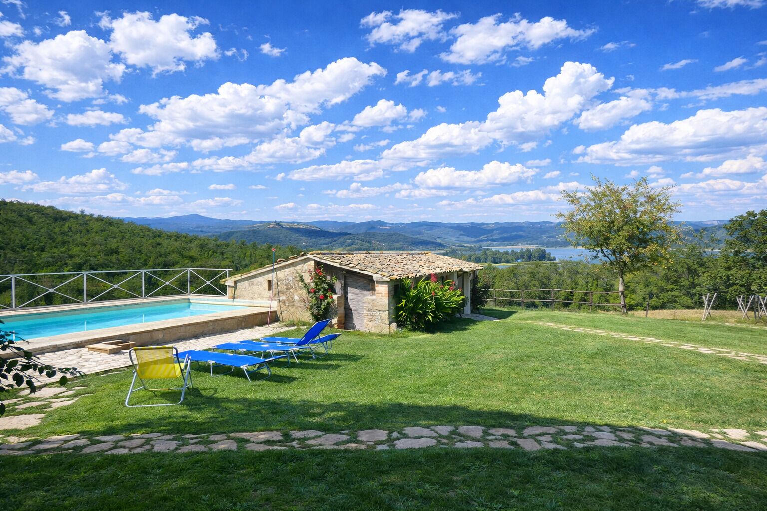 Un espace piscine avec des chaises longues, un bâtiment en pierre et une vue sur les montagnes et un lac.