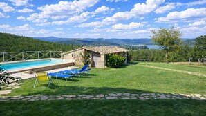 A pool area with lounge chairs, a stone building, and a view of mountains and a lake. - SCAPPO IN UMBRIA, Casale al Lago (Baschi)