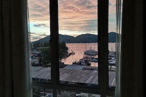 Un port de plaisance avec des bateaux amarrĂ©s, une montagne en arriĂšre-plan et une vue Ă travers une fenĂȘtre avec des rideaux.