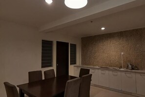A dining area with a rectangular table and six chairs, a kitchen with a patterned backsplash, and a ceiling with recessed lighting. - Spacious & Homey Apartment at Marina Island by JoMy Homestay (Manjung)