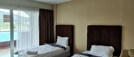 Una habitación de hotel con dos camas, un ventanal con cortinas y vistas al exterior.