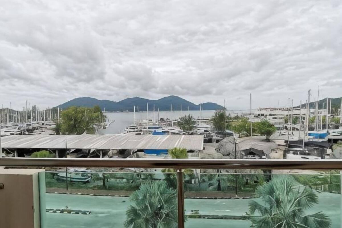 A marina with boats, a mountain in the background, and a view through a window with a balcony.