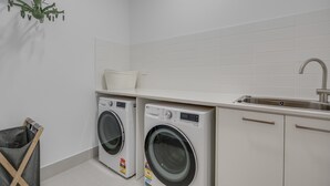 A laundry room with two front-loading washing machines, a sink, and a drying rack. - Oceanview Luxury With Dedicated Workspace (Adelaide)