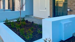 A modern building with a flat roof, large windows, and a brick facade. There are rectangular planters with small plants and a clear sky visible through the windows. - Oceanview Luxury With Dedicated Workspace (Adelaide)