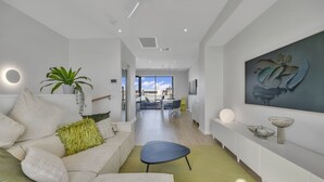 A modern living room with a sofa, a coffee table, and a dining area in the background. - Oceanview Luxury With Dedicated Workspace (Adelaide)