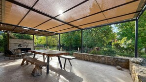 Une terrasse extérieure avec une table et des bancs en bois, des murs en pierre et une vue sur une végétation luxuriante.