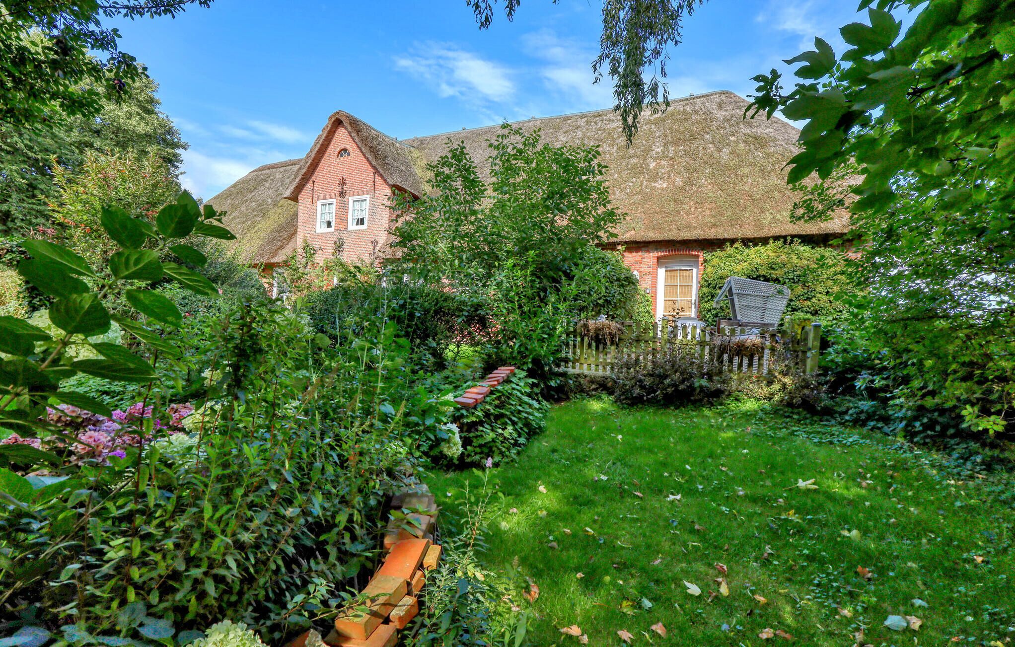 A traditional house with a thatched roof, surrounded by lush greenery and a well-maintained garden.