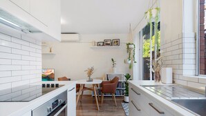 A modern kitchen with white cabinetry, a dining area with a table and chairs, and a built-in oven. - Snug St Kilda Apartment With Private Courtyard (Melbourne)